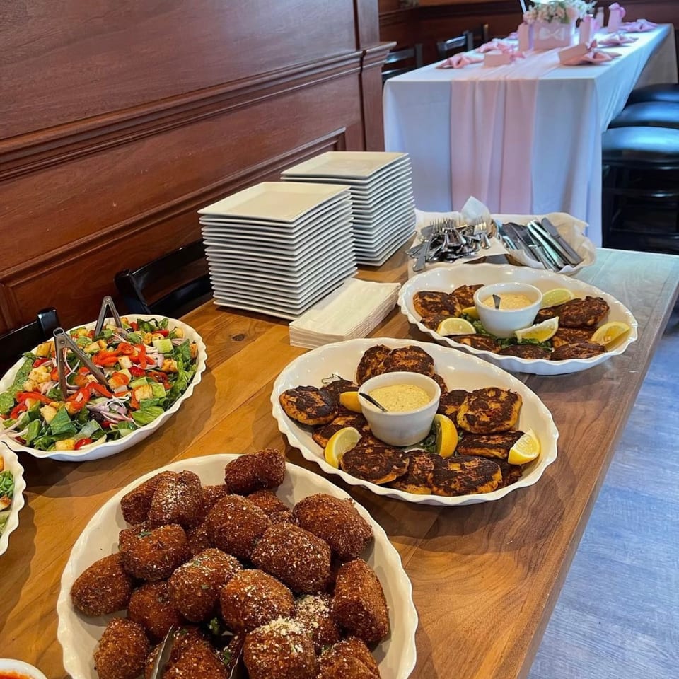 Buffet table with salad, crab cakes, and fried appetizers, with stacked plates and cutlery.