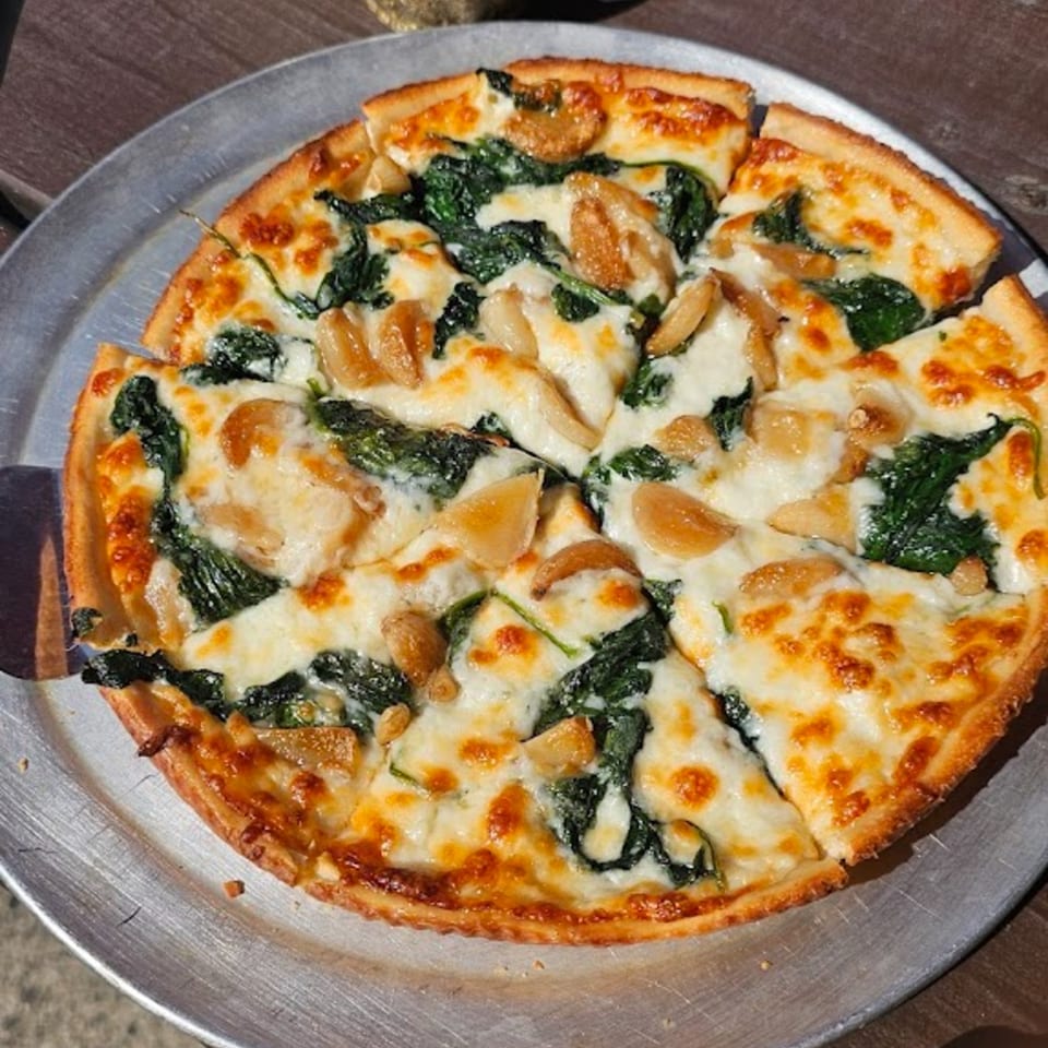 A Nanuet Restaurant pizza with spinach, roasted garlic, and melted mozzarella cheese on a metal pan.