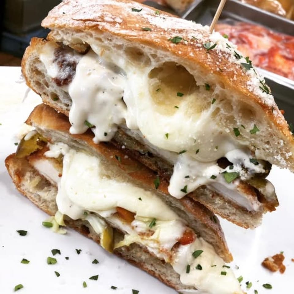 A Nanuet Restaurant sandwich, cut in half, overflowing with melted cheese and topped with herbs.