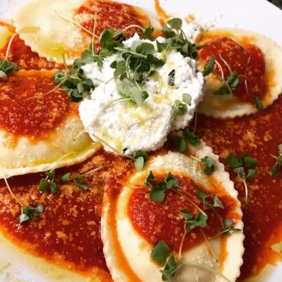Nanuet Restaurant's ravioli with red sauce, ricotta cheese, and microgreens on a white plate.