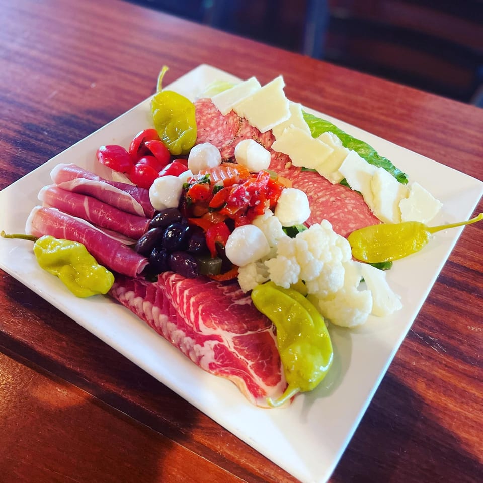 A white rectangular plate filled with various Italian meats, cheeses, olives, and pickled vegetables.