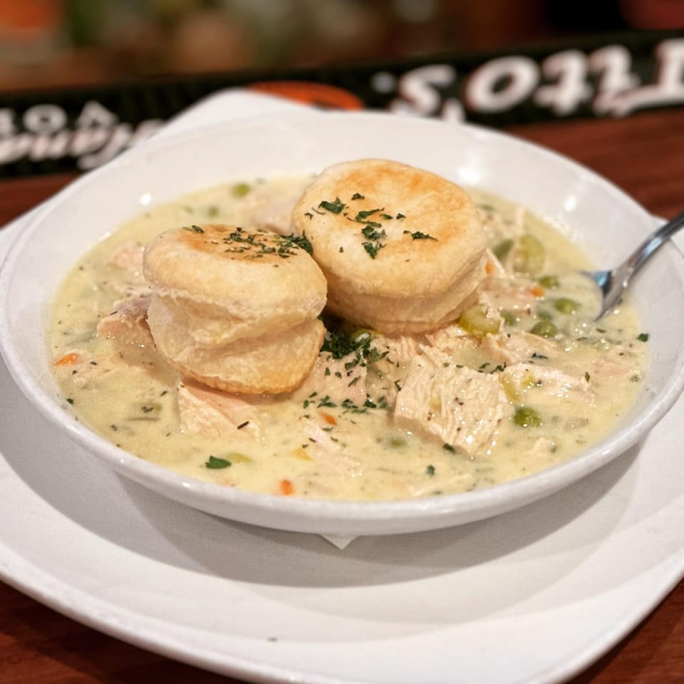 Creamy chicken pot pie with vegetables and two biscuits, garnished with parsley, in a white bowl.