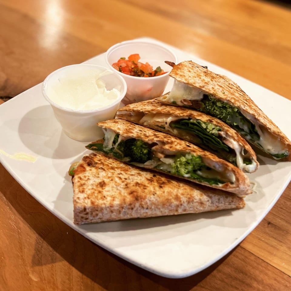 Four quesadilla wedges with melted cheese, broccoli, and spinach, served with salsa and sour cream.