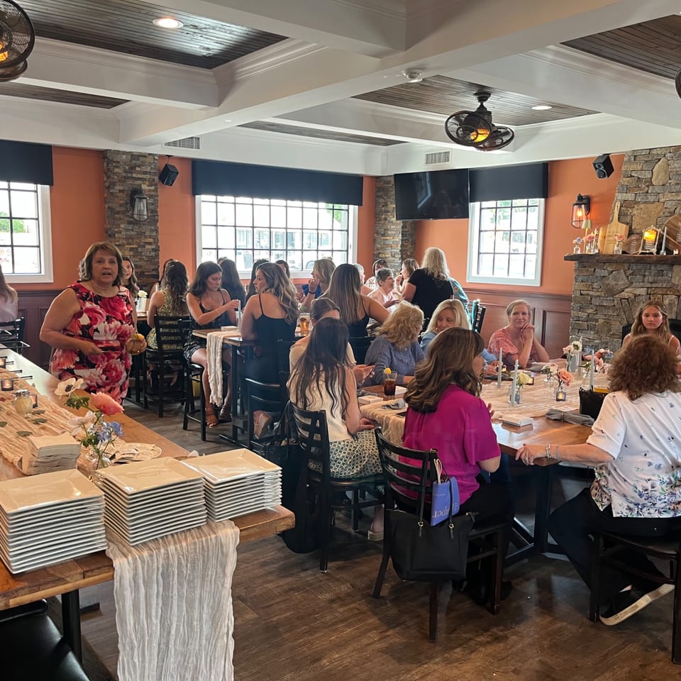 Women gather at Nanuet Restaurant, seated at tables with plates and drinks, enjoying a social event.