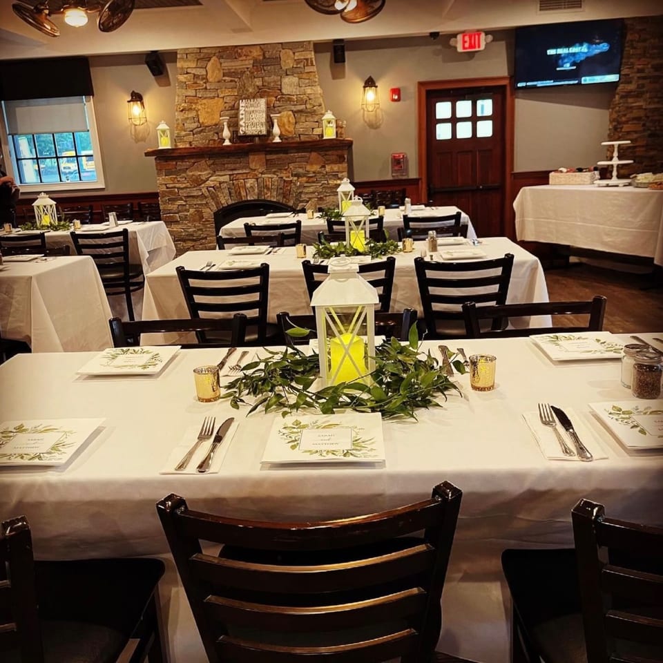 Restaurant dining room set for an event with white tablecloths, lanterns, and greenery centerpieces.