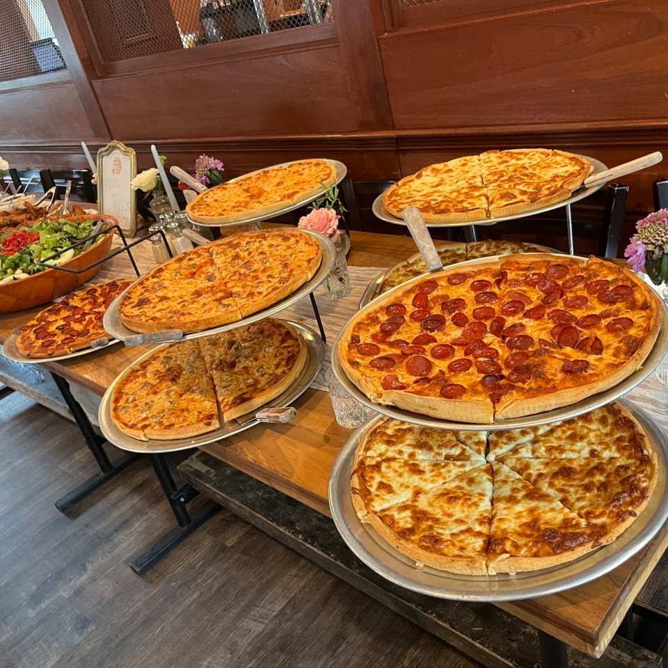 A buffet table laden with various Nanuet Restaurant pizzas, including pepperoni, cheese, and sausage.