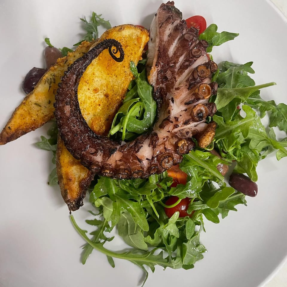 Grilled octopus and potato wedges on a bed of arugula with cherry tomatoes and olives.